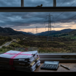 Legal papers and a calculator by a window overlooking pylons in Scottish hills, illustrating an energy tax ruling