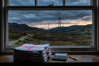 Legal papers and a calculator by a window overlooking pylons in Scottish hills, illustrating an energy tax ruling